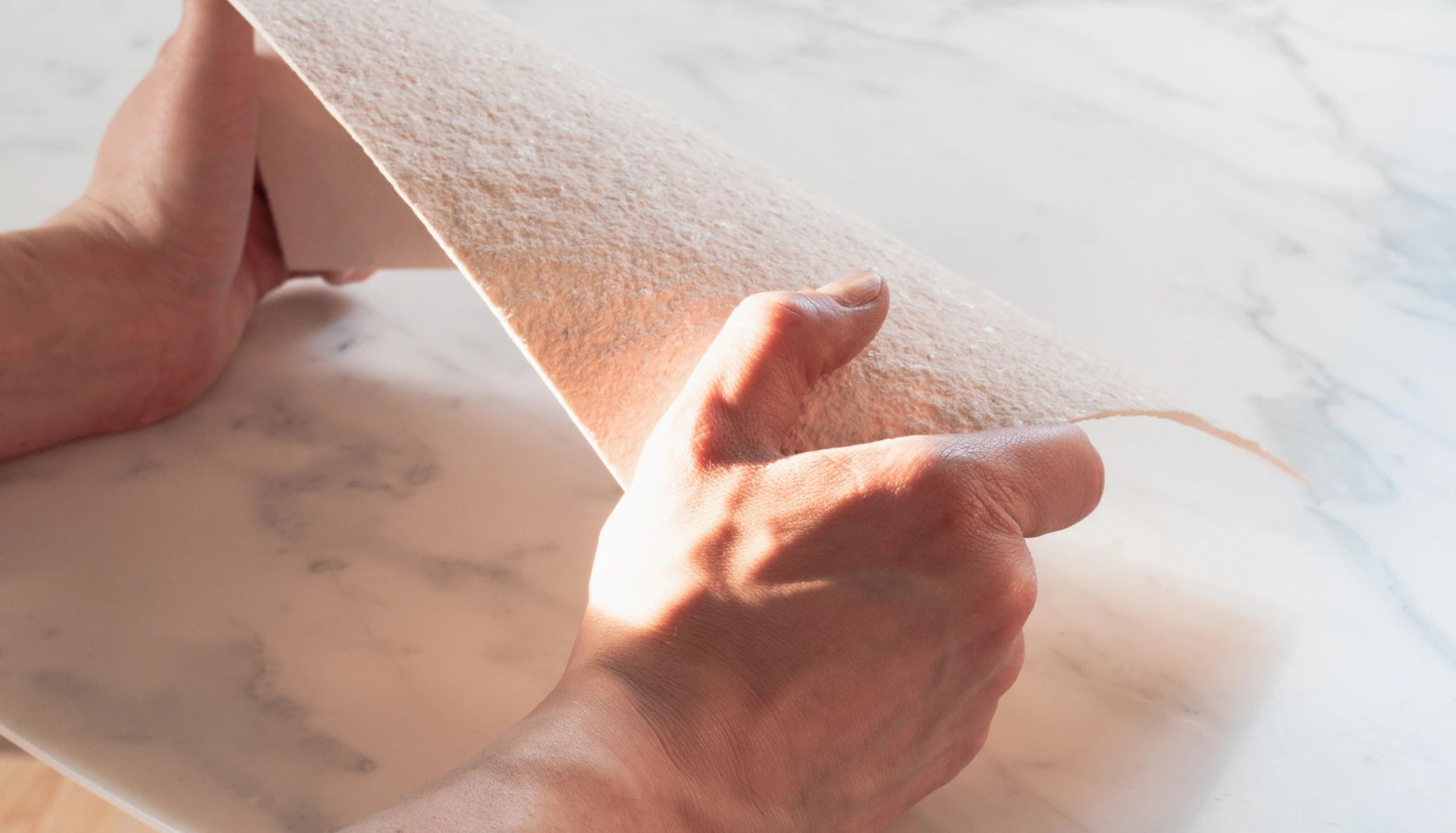 Hände halten eine dünne, flexible Platte aus hellem Sandstein, die zur Veredelung von stonearts® Akustikpaneelen und dekorativen Wandverkleidungen verwendet wird, ideal für moderne und nachhaltige Innenraumlösungen.